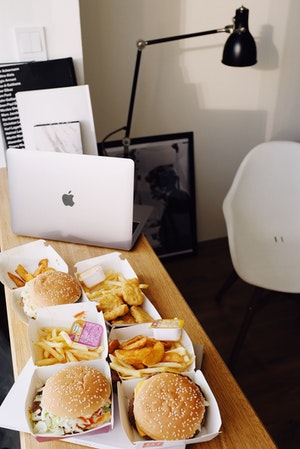 Picture of takeout containers filled with french fries, burgers, and chicken nuggets sitting on a desk beside a laptop