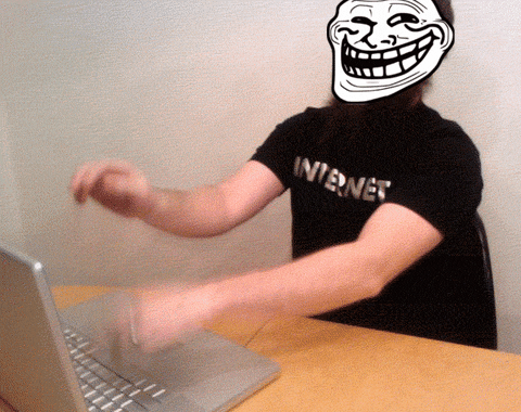 A person with a cartoon Internet-troll face angrily types on their laptop's keyboard